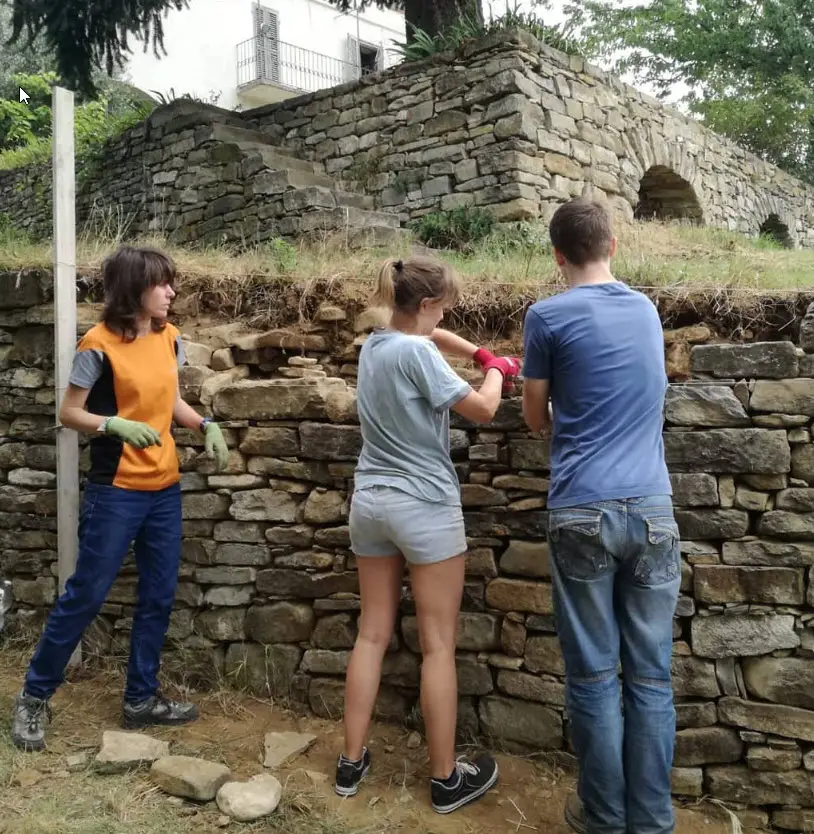 Volontari europei che dedicano 2 settimane delle loro vacanze a sostenere progetti di utilità pubblica. In questo caso in un progetto con l'obiettivo di ricostruzione dei muri in pietra a secco e pulizia dalla vegetazione cresciuta in eccesso a Monteoliveto. Camp leader Donatella Murtas (immagine tratta da Ecomusei dei Terrazzamenti).